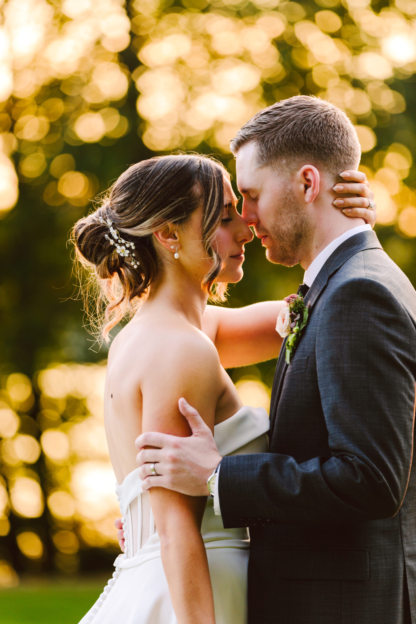 Bride and groom embracing nose to nose outdoors golden bokeh lights glowing behind them