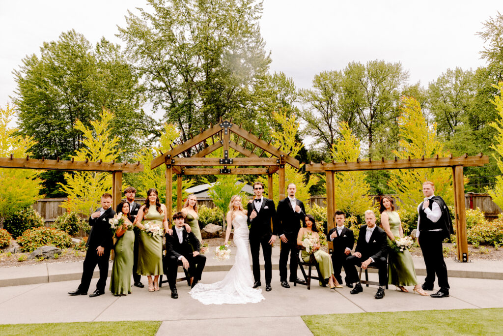 Liljebeck farms snohomish wedding venue guide Wedding party portrait on the outdoor patio at liljebeck farms with bridesmaids in sage green gowns groomsmen in black tuxedos and the couple centered beneath a wood pergola surrounded by fall foliage liljebeck farms snohomish wedding venue guide