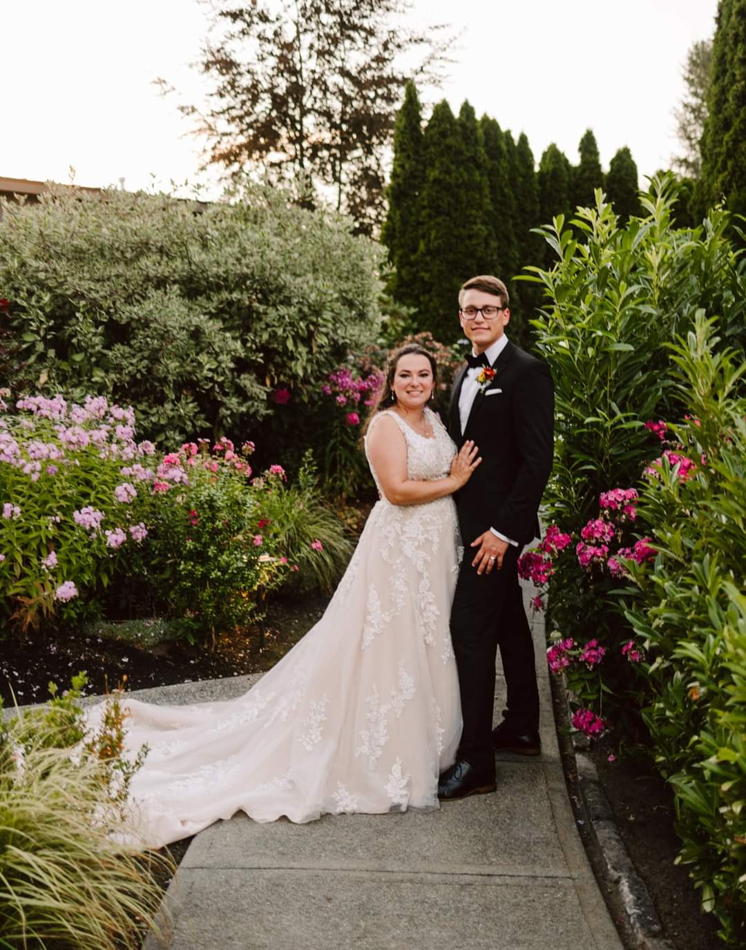 Bride and groom in a garden, posing together in wedding attire with flowers all around them.