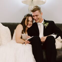 Smiling bride and groom sitting together on a leather sofa reading cards on their wedding day