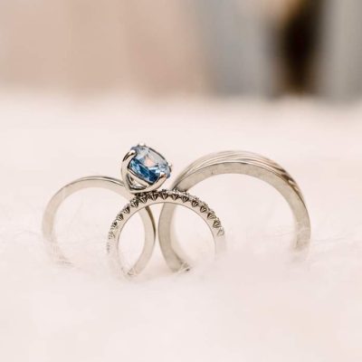 Two silver rings with a blue gemstone engagement ring resting on a soft white surface.