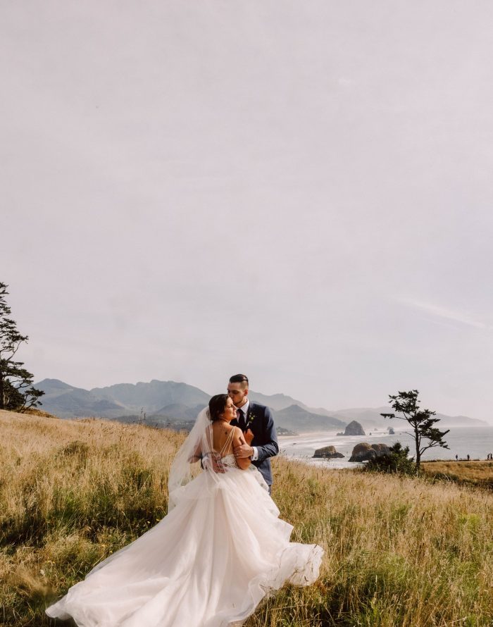 Cannon Beach Oregon Wedding GSquared Weddings Photography A bride and groom embrace in a grassy field with mountains and the ocean in the background. Perfect for couples seeking intimate moments, this serene, romantic scene captures the essence of elopement prices and unforgettable memories