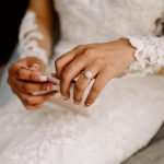 Close-up of a bride's hands adjusting her ring, with intricate lace sleeves in the background.