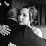 Close hug between a man and a woman; the woman's face shows a tear as they embrace, in black and white.